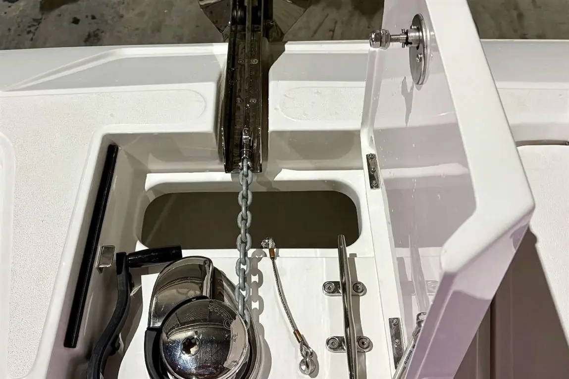 View of a boat storage compartment featuring an anchor chain, a winch, and various metal fittings on a white surface.